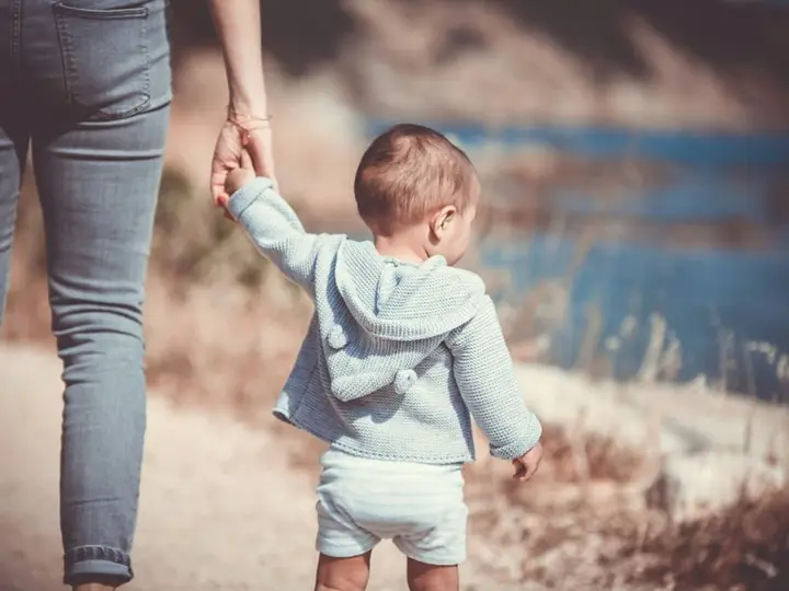 A small child holding an adult's hand on a walk