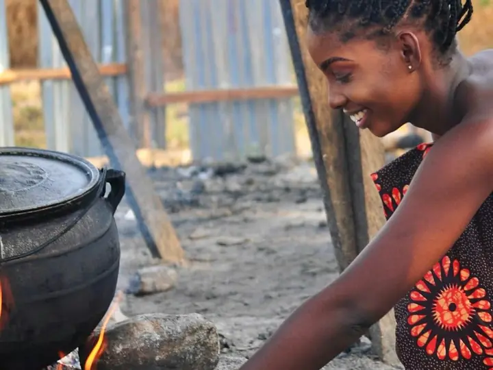 A smiling woman cooking over a fire