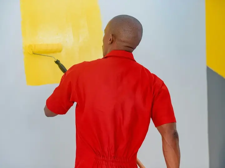 A painter rolling yellow paint on a wall